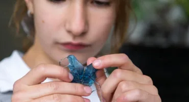Close-up of hands holding a blue translucent dental retainer with metal wires.