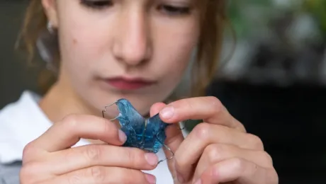 Close-up of hands holding a blue translucent dental retainer with metal wires.