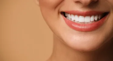 Close-up of a person smiling, showing white teeth and pink lips against a warm beige background.