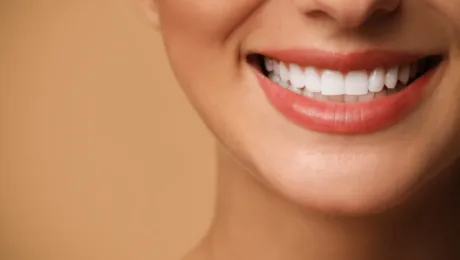 Close-up of a person smiling, showing white teeth and pink lips against a warm beige background.